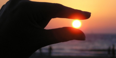 Dedos índice y pulgar "sosteniendo" al sol en el atardecer.