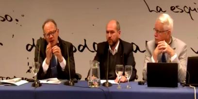 Fotografía de tres hombres sentados uno al lado de otro en una mesa de conferencia. 