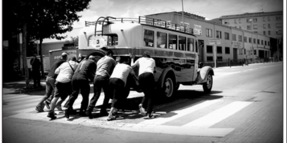 Foto en blanco y negro de un conjunto de personas empujando un ómnibus antiguo.