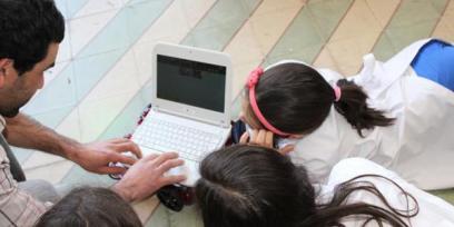 Fotografía de un docente y tres alumnos mirando una laptop.