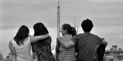 Fotografía de cuatroa dolescentes de espaldas, sentados en un muro. 