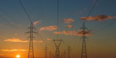 Puesta de sol, en el campo y se ven las torres de alta tensión que sostienen las redes eléctricas.