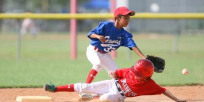 niño (corredor), barriendose para llegar a tocar una base, antes que la pelota llegue al niño en defensa