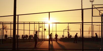 Imagen decorativa con un plano general de una cancha de basketball a contra luz del atardecer