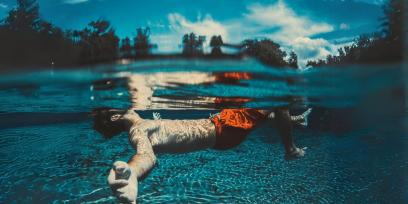 Hombre flotando en el agua, con los brazos extendidos. Cielo celeste con algunas nubes. 