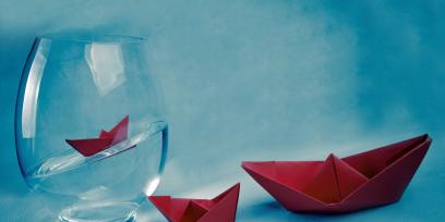 Vaso de vidrio con agua y tres barcos de papel plegado.