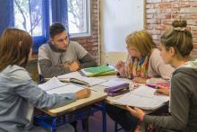Fotografía de tres estudiantes y un docente sentados alrededor de una mesa.