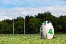 Imagen decorativa de una cancha de rugby con un primerisimo primer plano de una pelota y en el fondo la H o portería de rugby