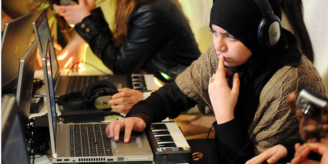 Niña trabajando con una computadora portátil y un teclado musical.