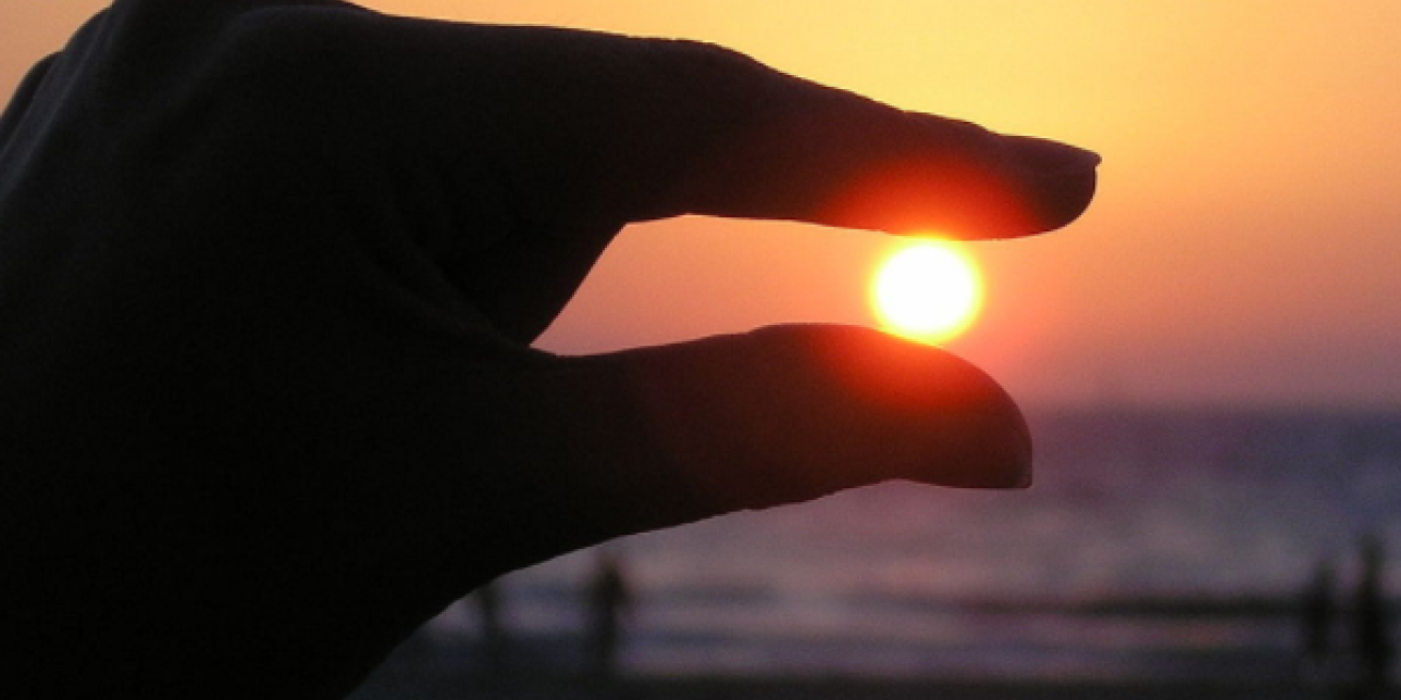 Dedos índice y pulgar "sosteniendo" al sol en el atardecer.