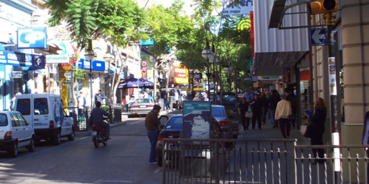 Fotografía de una calle donde se ven autos, motos y peatones. 