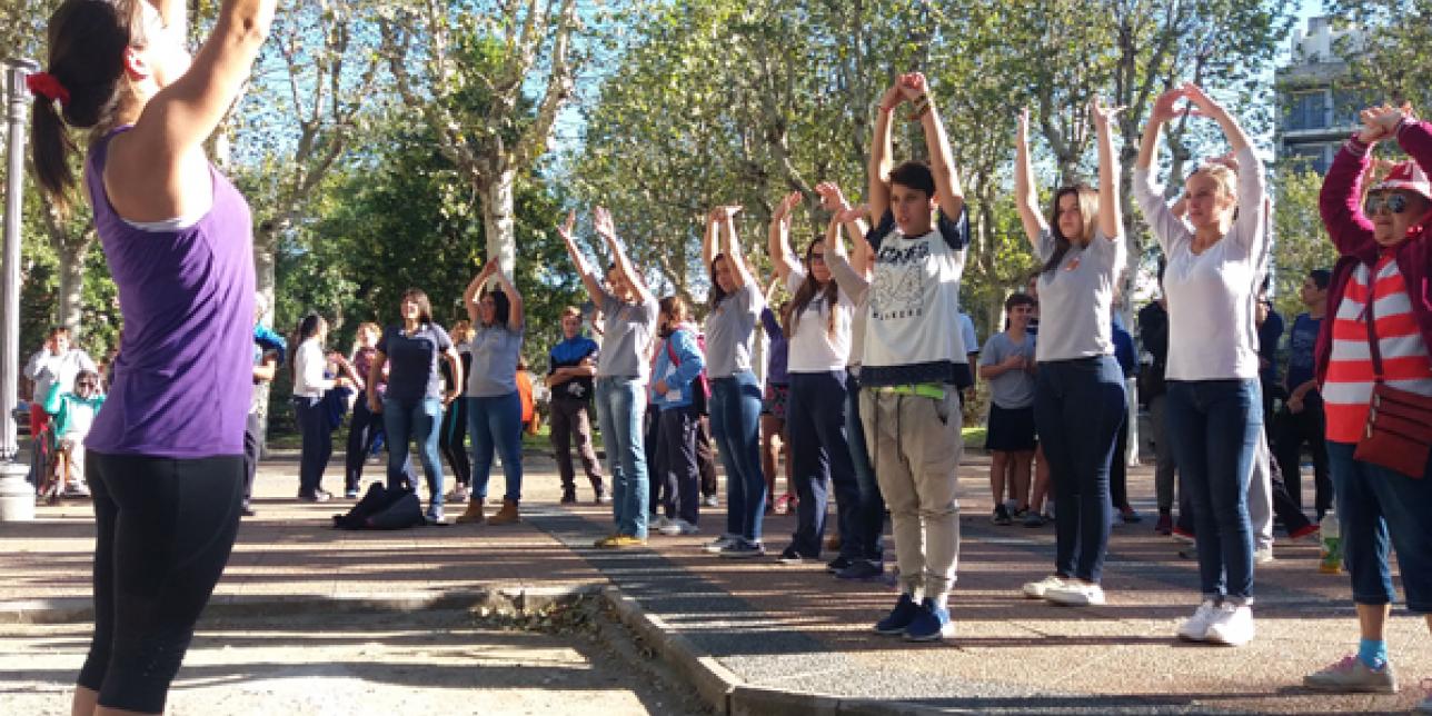 Fotografía de una profesora dirigiendo clase de gimnasia aeróbica en una plaza.