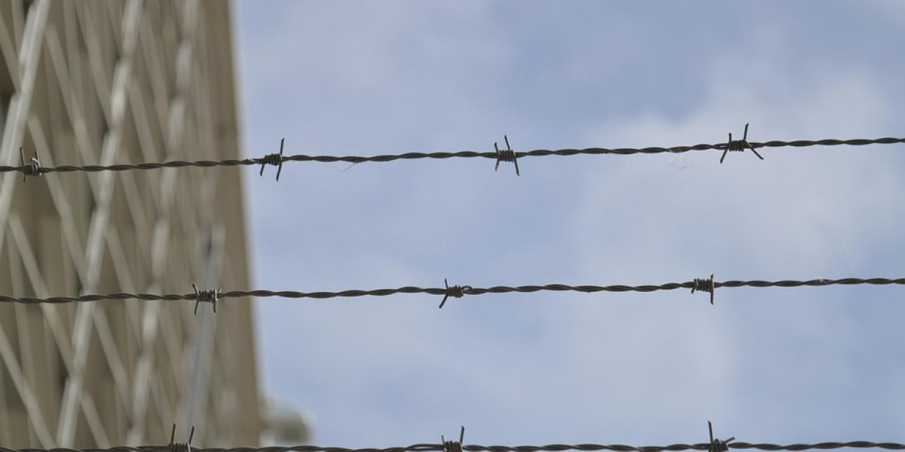 Imagen que muestra alambres de puas y en el fondo la imagen lejana de una cárcel y el cielo