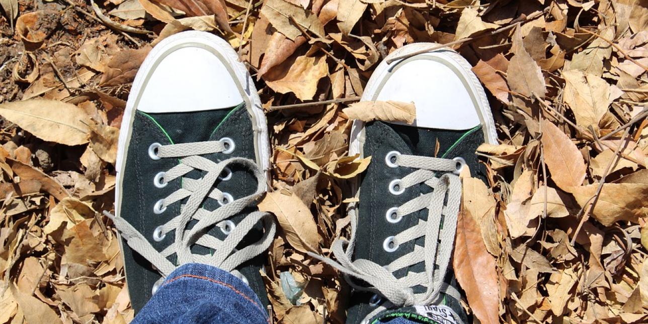 Imagen que muestra los pies de un chico que lleva puestos unos championes tipicos de uso adolescente. El suelo está cubierto por una alfombra de hojas de otoño