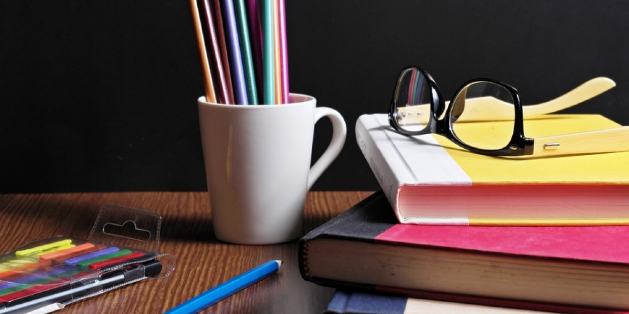 Libros sobre escritorio, con lápices, lentes y taza