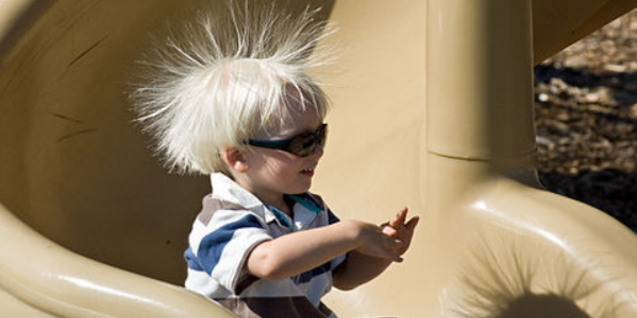 Niño bajando por un tobogán de plástico con sus cabellos electrizados, tiene los cabellos parados, repelidos por la fuerza eléctrica entre cargas de igual signo entre ellos.