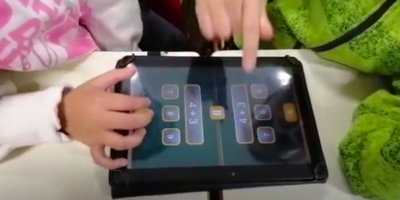 dupla de niños enfrentados con una tablet con la aplicación Math Duel sumando dígitos