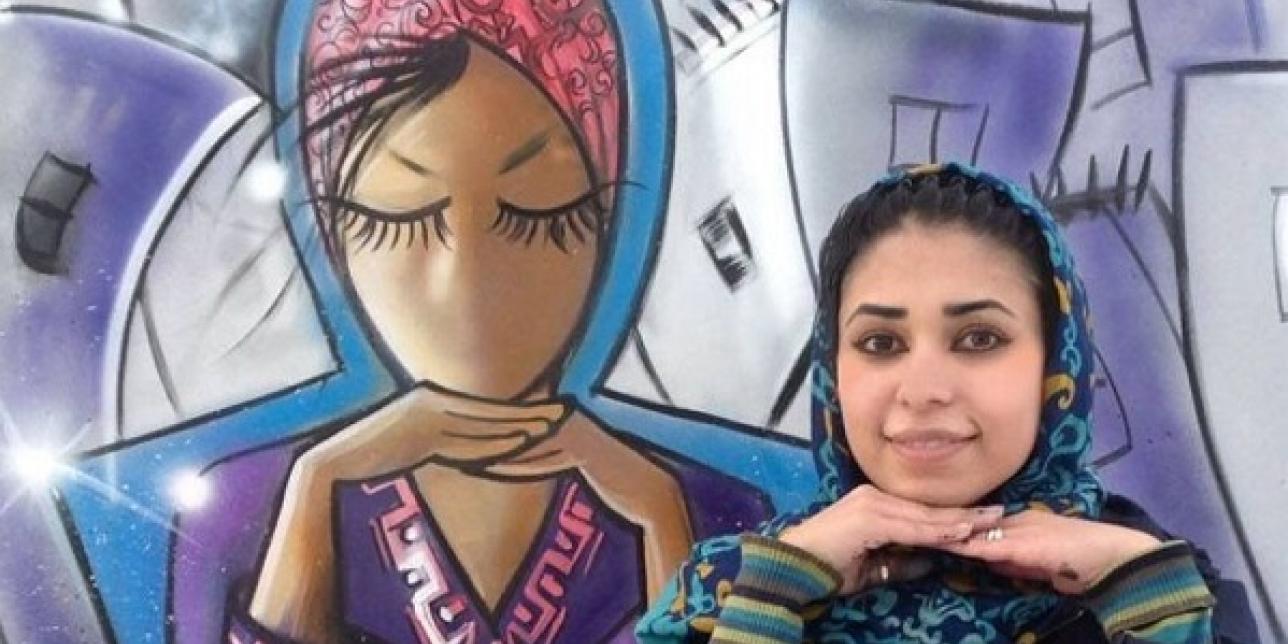 Fotografía de Shamsia Hassani y una de sus graffitis sobre una mujer afgana, la imagen tiene tonalidades lilas y celestes.
