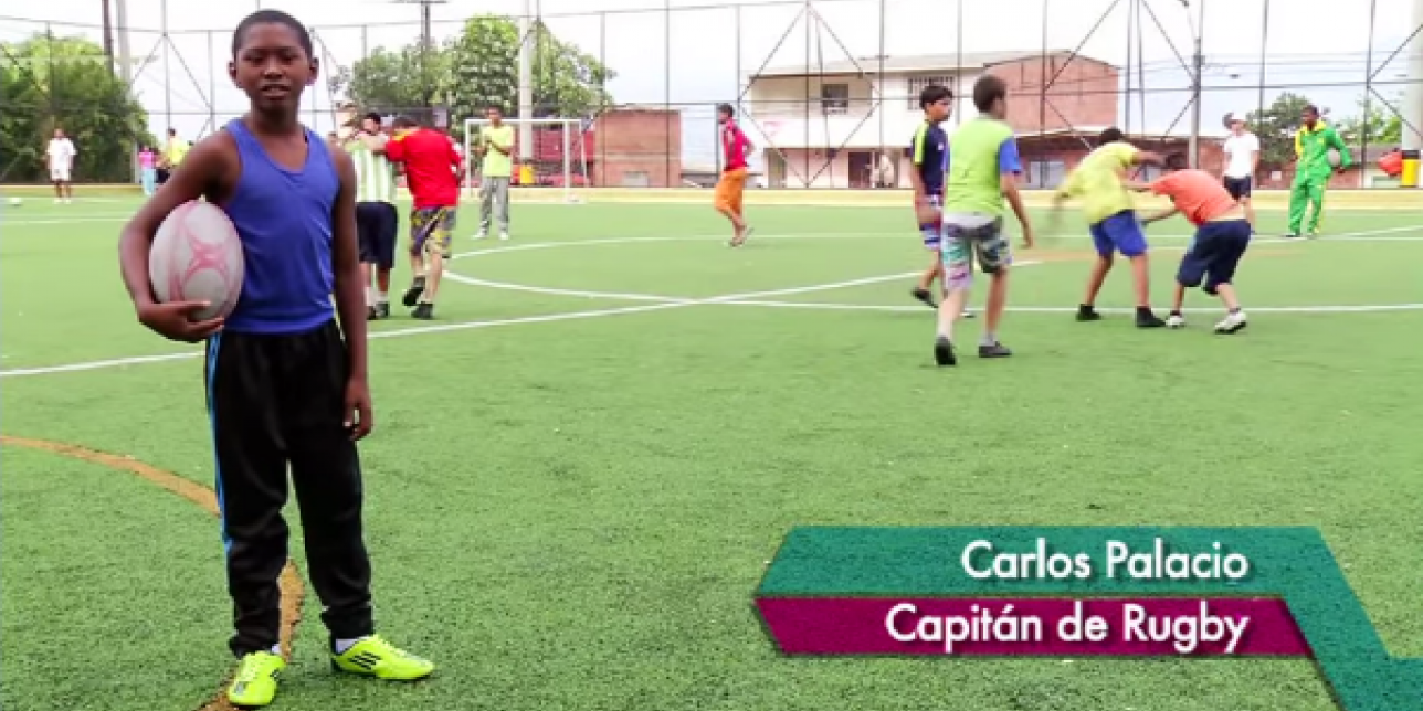 Carlo Palacio en primer plano con la ovalada bajo el brazo. De fondo sus compañeros practicando rugby