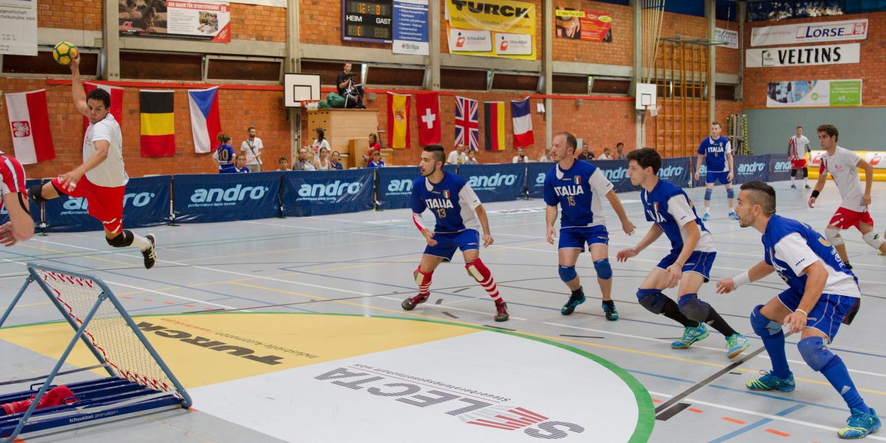 Se muestra al equipo rojo en posición de lanzar sobre el marco y el equipo azul con cuatro jugadores en postura defensiva para intentar atrapar la pelota luego del rebote.