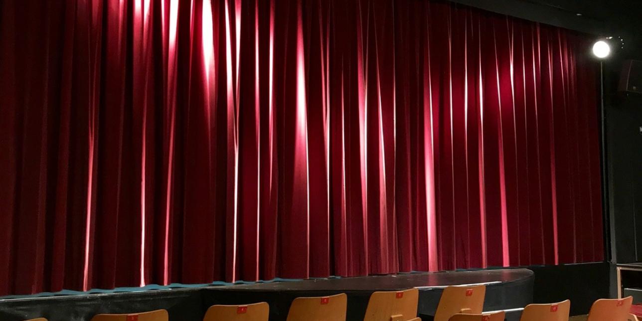 Cortina roja en sala de teatro iluminada con dos focos de luz blanca. 
