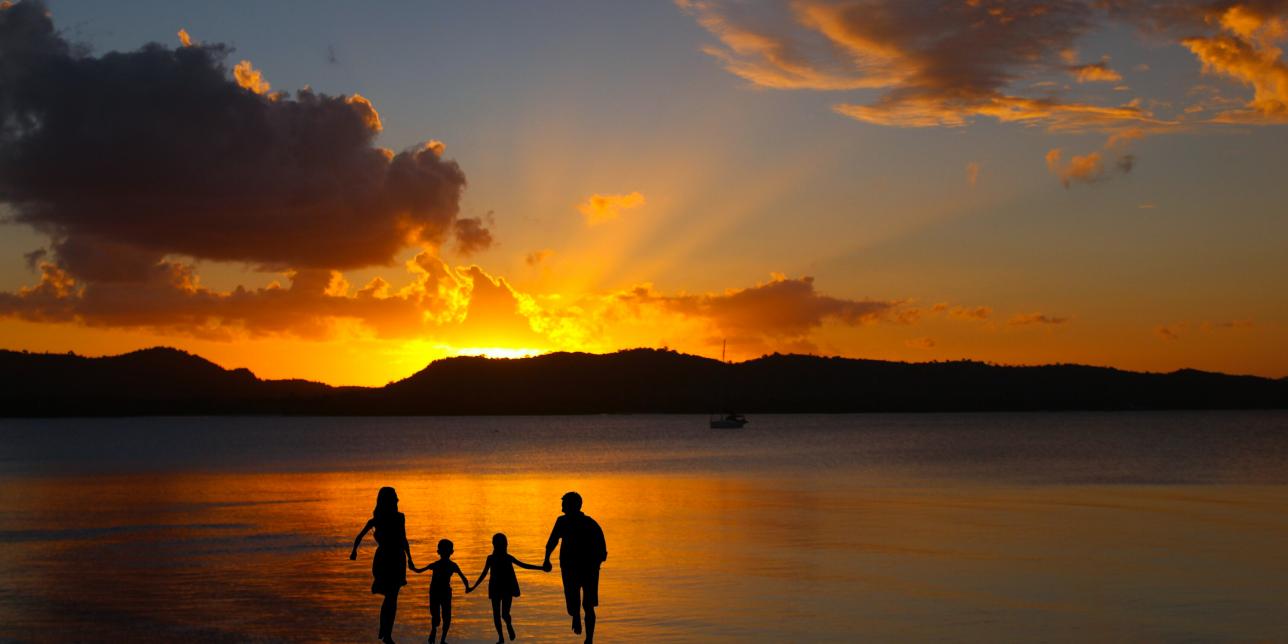 Siluetas de una familia con una puesta de sol en la costa