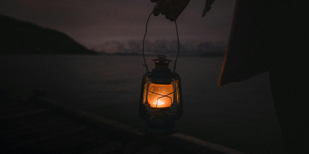 Farol encendido colgando de una mano en espacio abierto nocturno