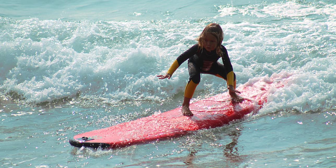 Niño surfeando una ola pequeña con una tabla de aprendizaje